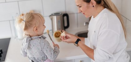 A mother and her young daughter interact while preparing food in a modern kitchen.