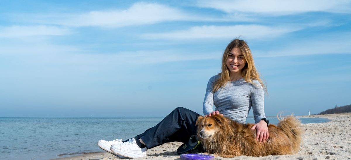 Woman enjoying a sunny day on Kołobrzeg beach with her dog, capturing the essence of leisure and companionship.