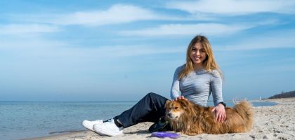 Woman enjoying a sunny day on Kołobrzeg beach with her dog, capturing the essence of leisure and companionship.