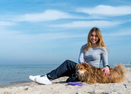 Woman enjoying a sunny day on Kołobrzeg beach with her dog, capturing the essence of leisure and companionship.